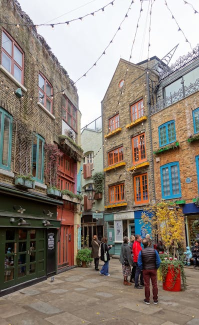 A vibrant outdoor courtyard surrounded by multi-story buildings with colorful, eclectic window frames painted in shades of blue, orange, and green. The buildings feature a mix of brick and plaster ext